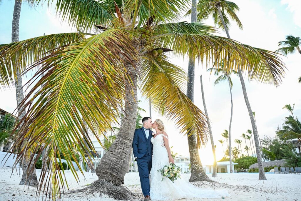 Bride and groom kissing below palm tree