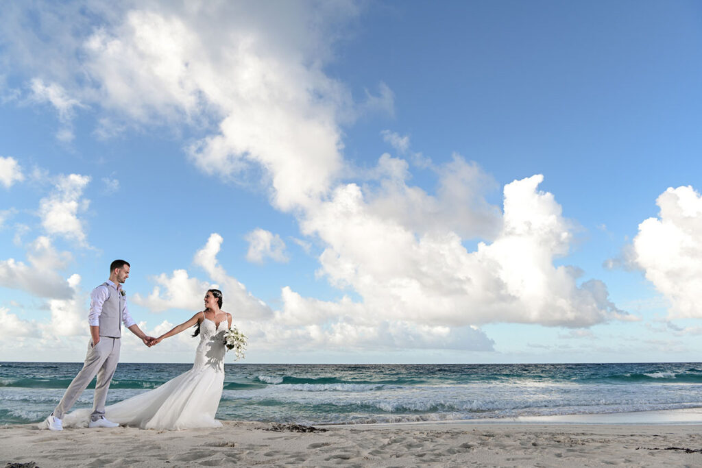 Bride is holding and leading groom on a beach