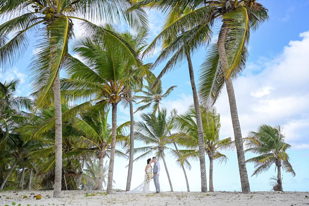 Bride and groom kissing below palm trees