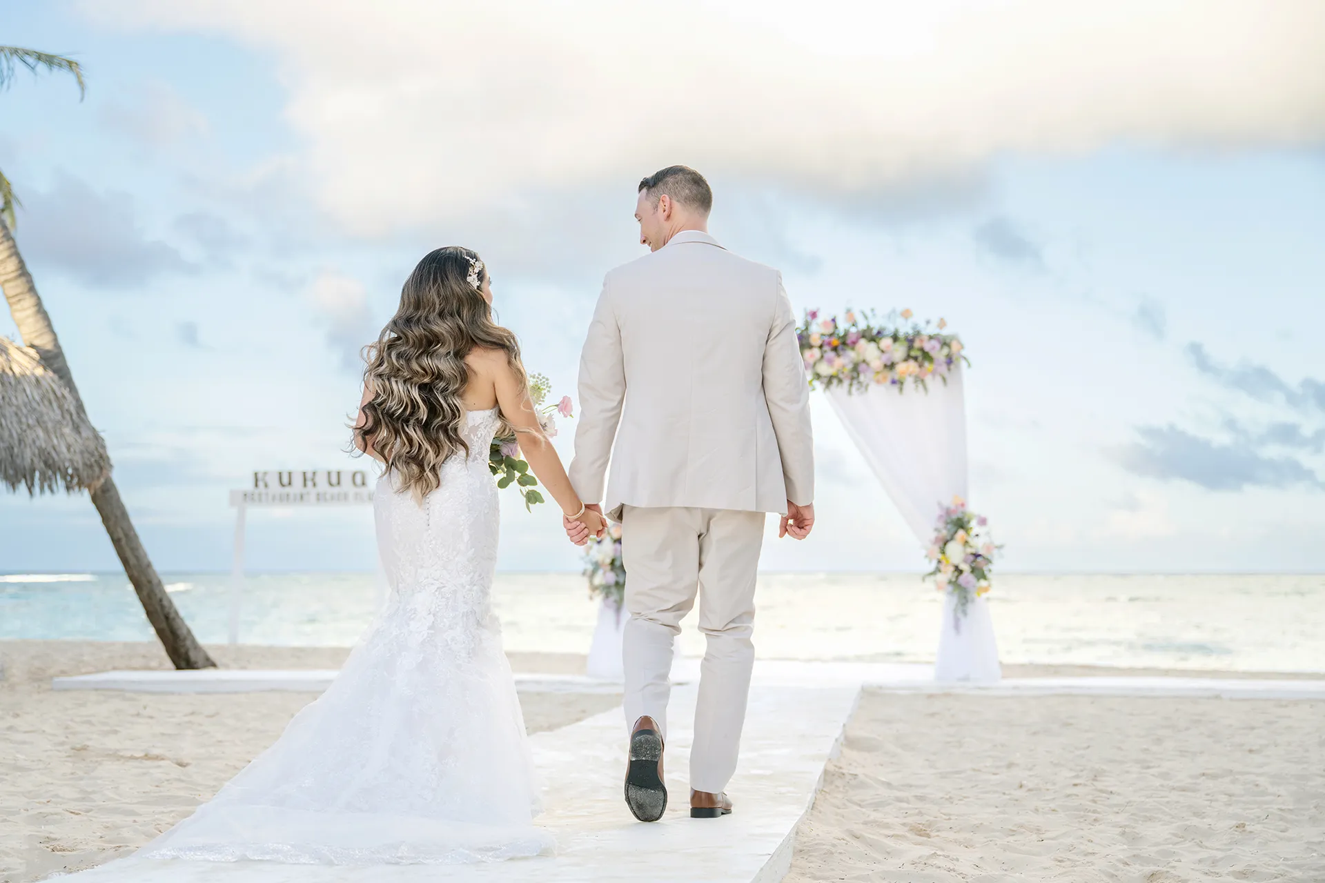 Cassandra and Matthew beneath a garden-inspired floral arch at Kukua Beach Club Cassandra and Matthew beneath a garden-inspired floral arch at Kukua Beach Club