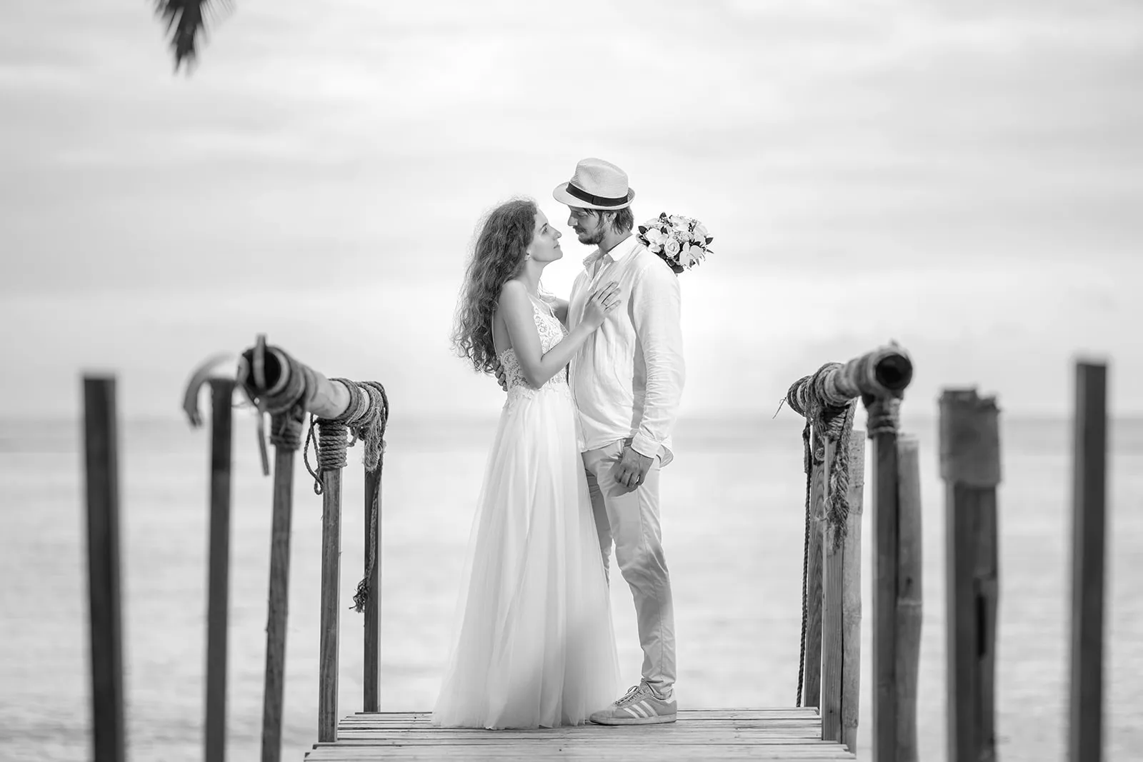 Black-and-white portrait of a couple in wedding attire on a wooden pier during a Punta Cana post-wedding session