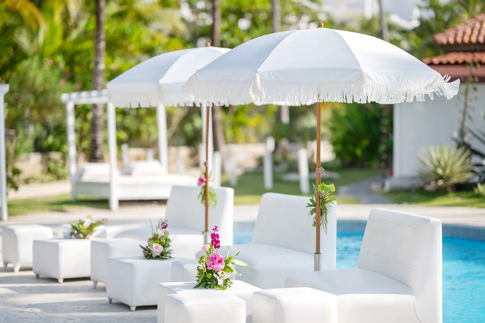 White lounge furniture and fringed umbrellas set up by the pool at Kukua Beach Club