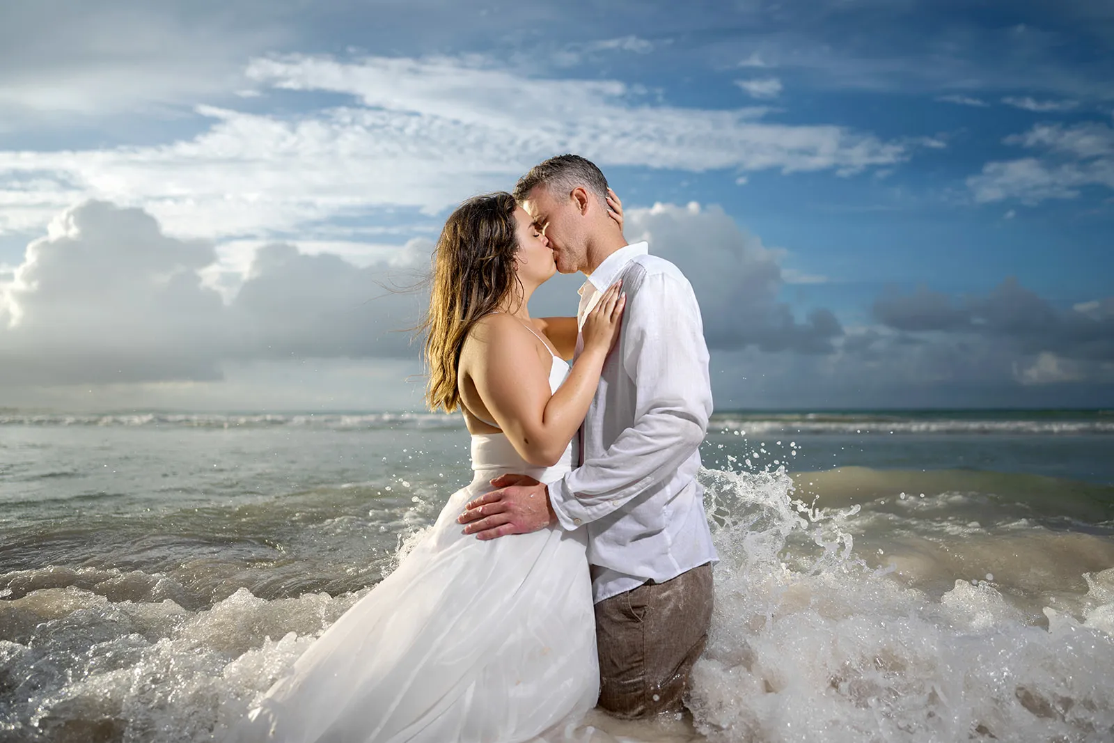 Couple kissing waist-deep in the sea as waves break around them during a Punta Cana Trash the Dress shoot Couple kissing waist-deep in the sea as waves break around them during a Punta Cana Trash the Dress shoot