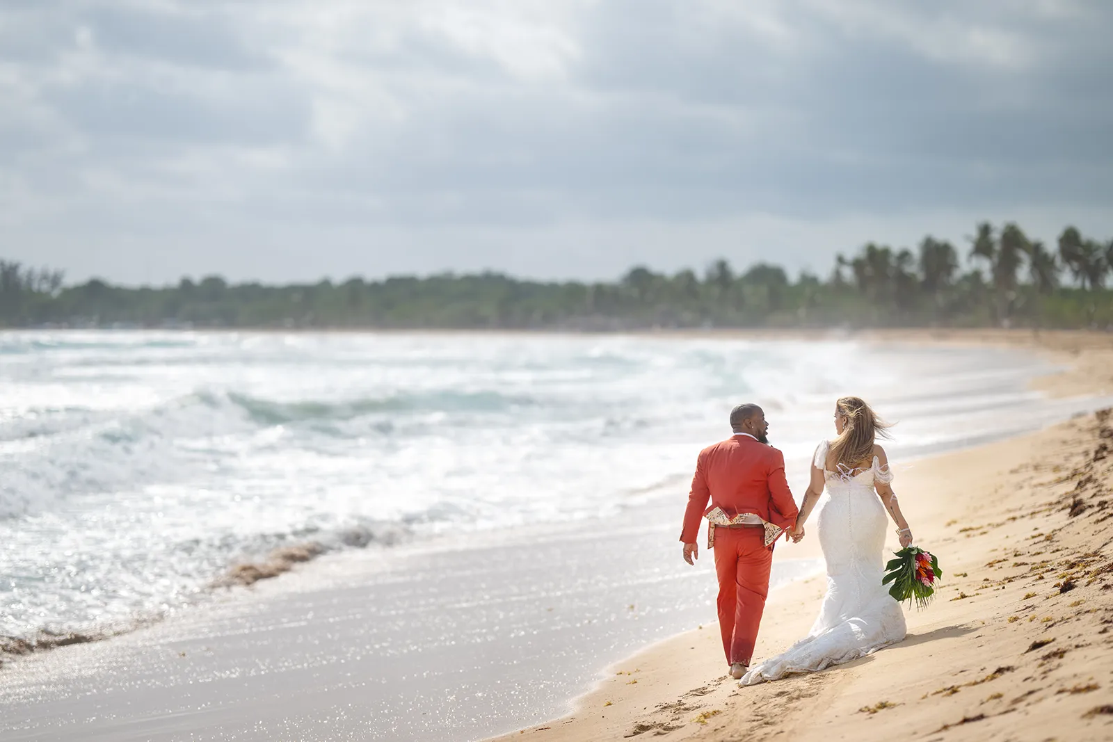 Newlyweds walking along the shoreline as waves roll in during a Trash the Dress session in Punta Cana