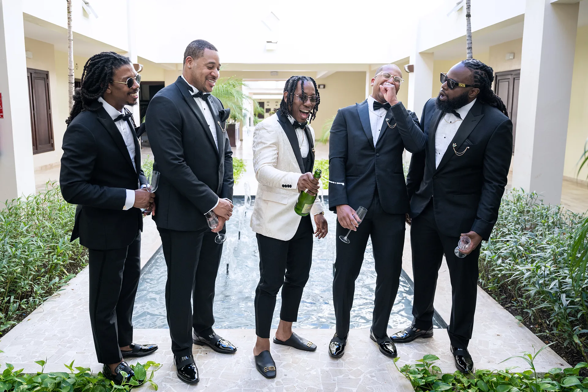 Groom in an ivory jacquard dinner jacket celebrating with groomsmen in black tuxedos at a Punta Cana resort