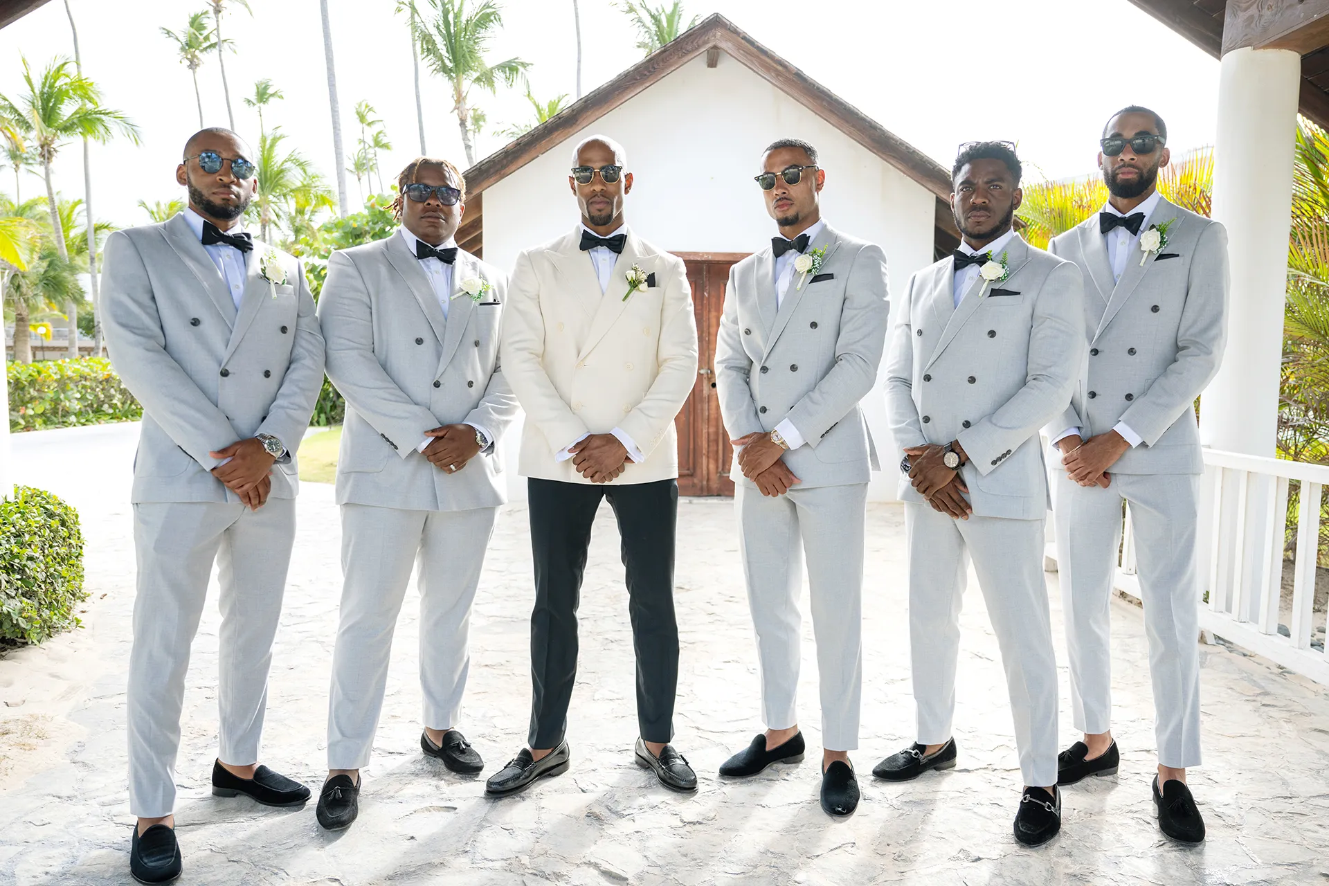 gray-groomsmen-suits-white-groom-jacket Groom in an ivory double-breasted jacket with groomsmen in light gray suits, black bow ties and white boutonnieres