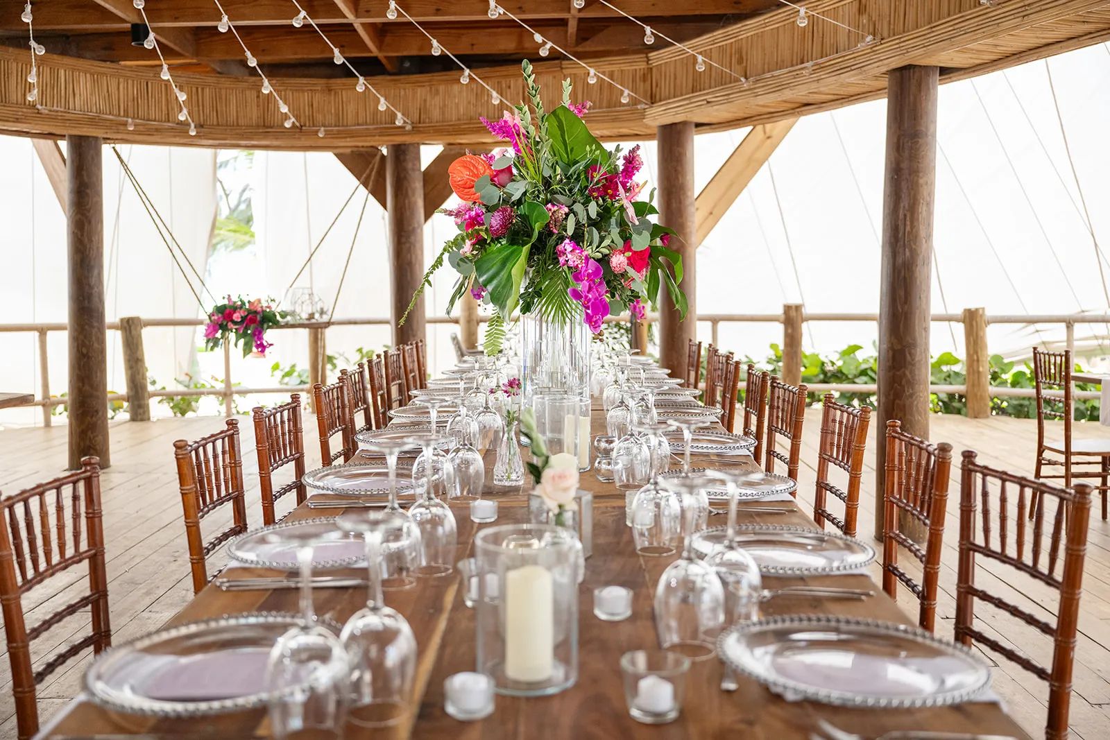 jellyfish restaurant reception decor Long wooden reception table with tropical pink centerpieces under the thatched roof at Jellyfish Restaurant