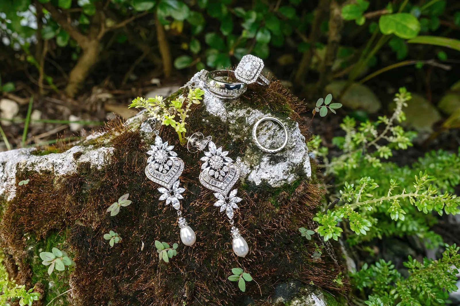 Quiana's wedding rings and bridal earrings photographed on a mossy rock before the Kukua Beach Club ceremony