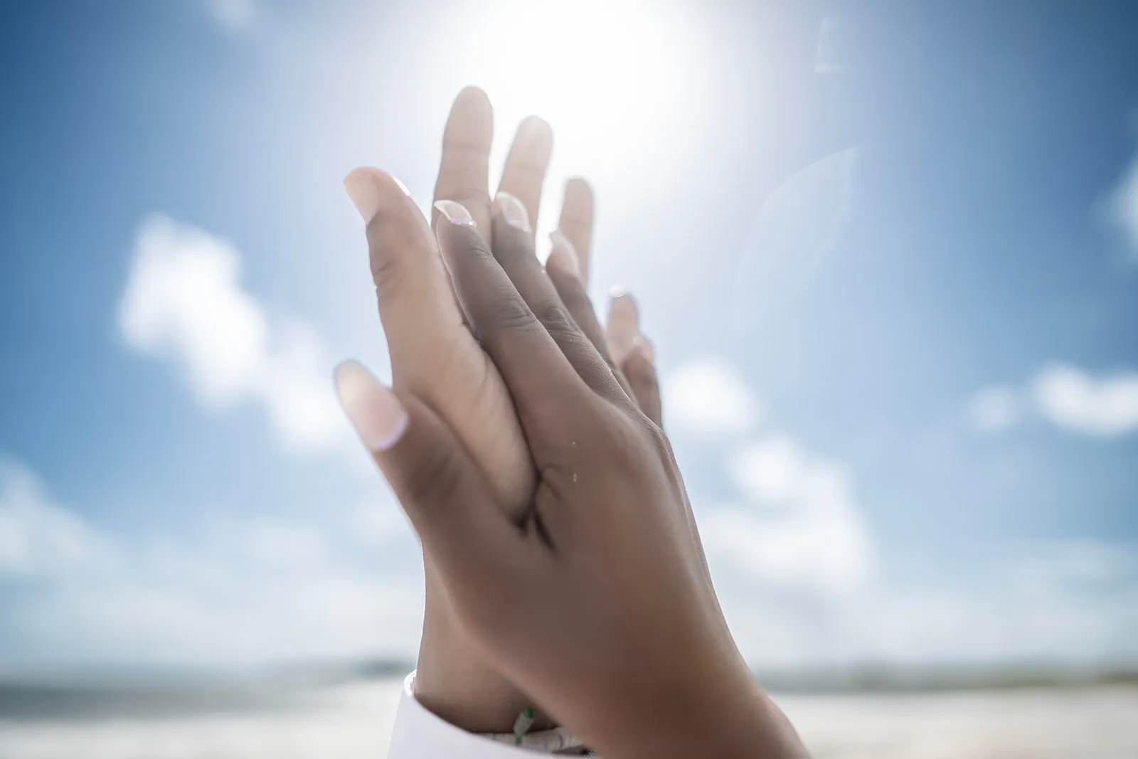 Quiana and Julio's hands with their wedding rings held up against the Caribbean sky