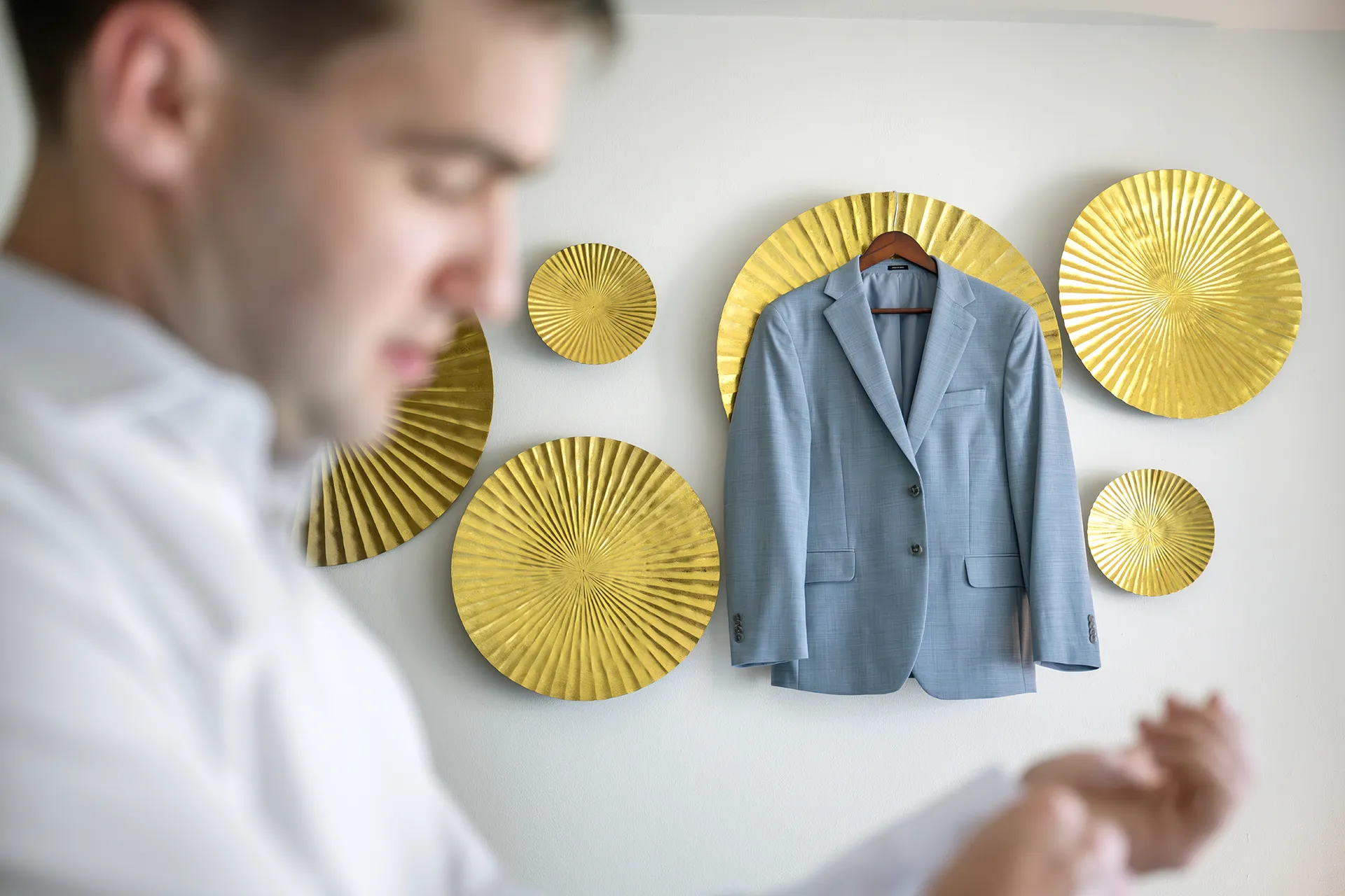 Lightweight light blue groom's jacket hanging on the wall while the groom gets ready