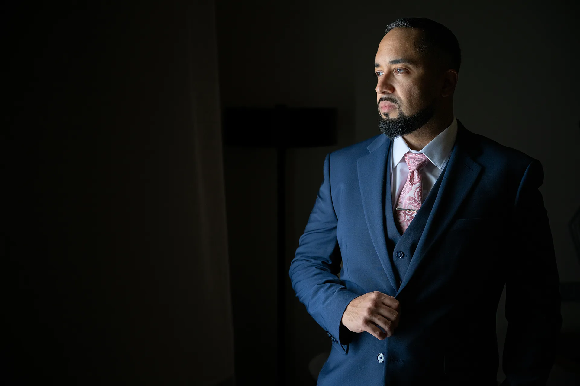 Groom in a navy three-piece suit with a pink paisley tie and tie bar before his Punta Cana wedding