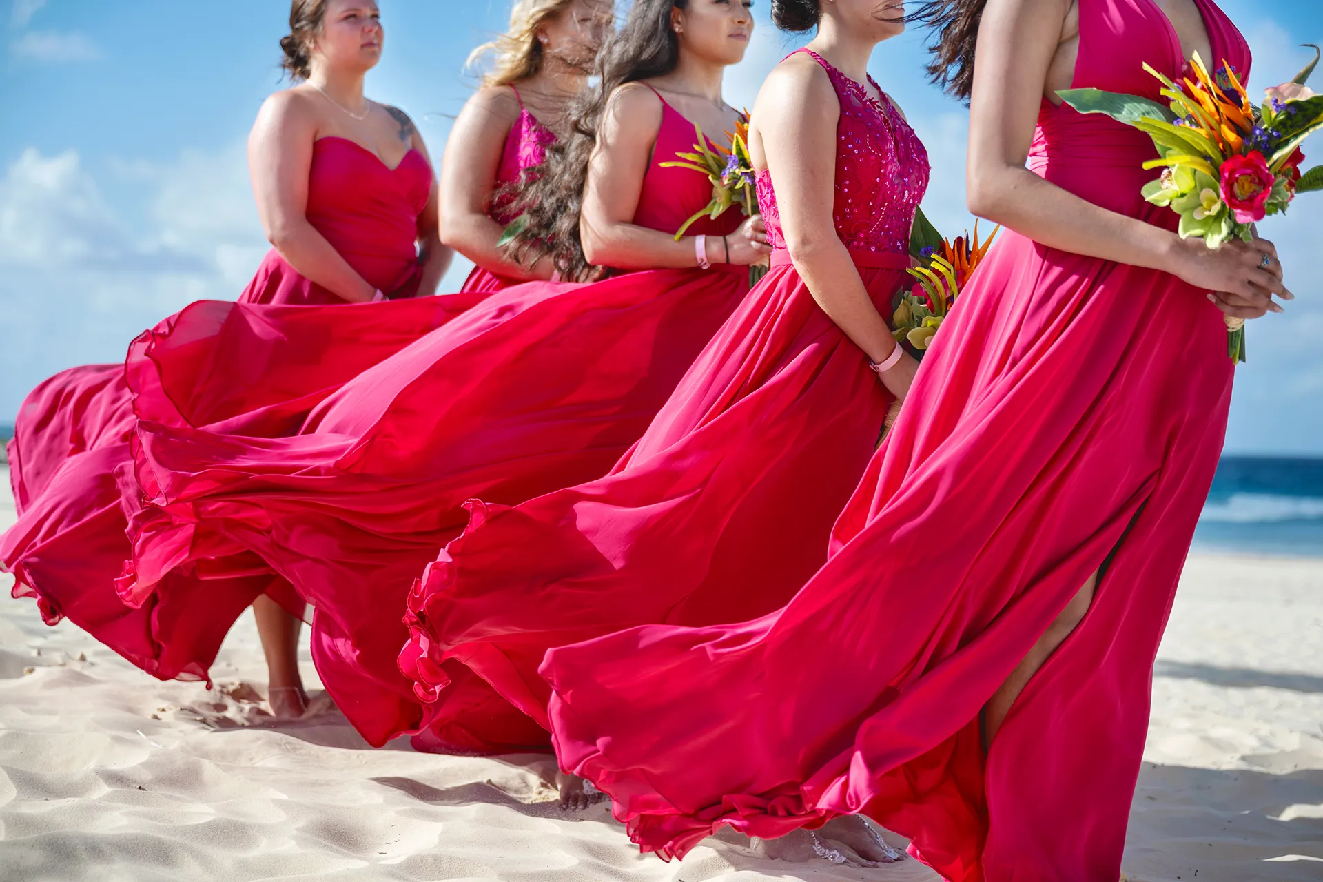 Bridesmaids in fuchsia chiffon dresses with skirts lifted by the breeze on a Punta Cana beach