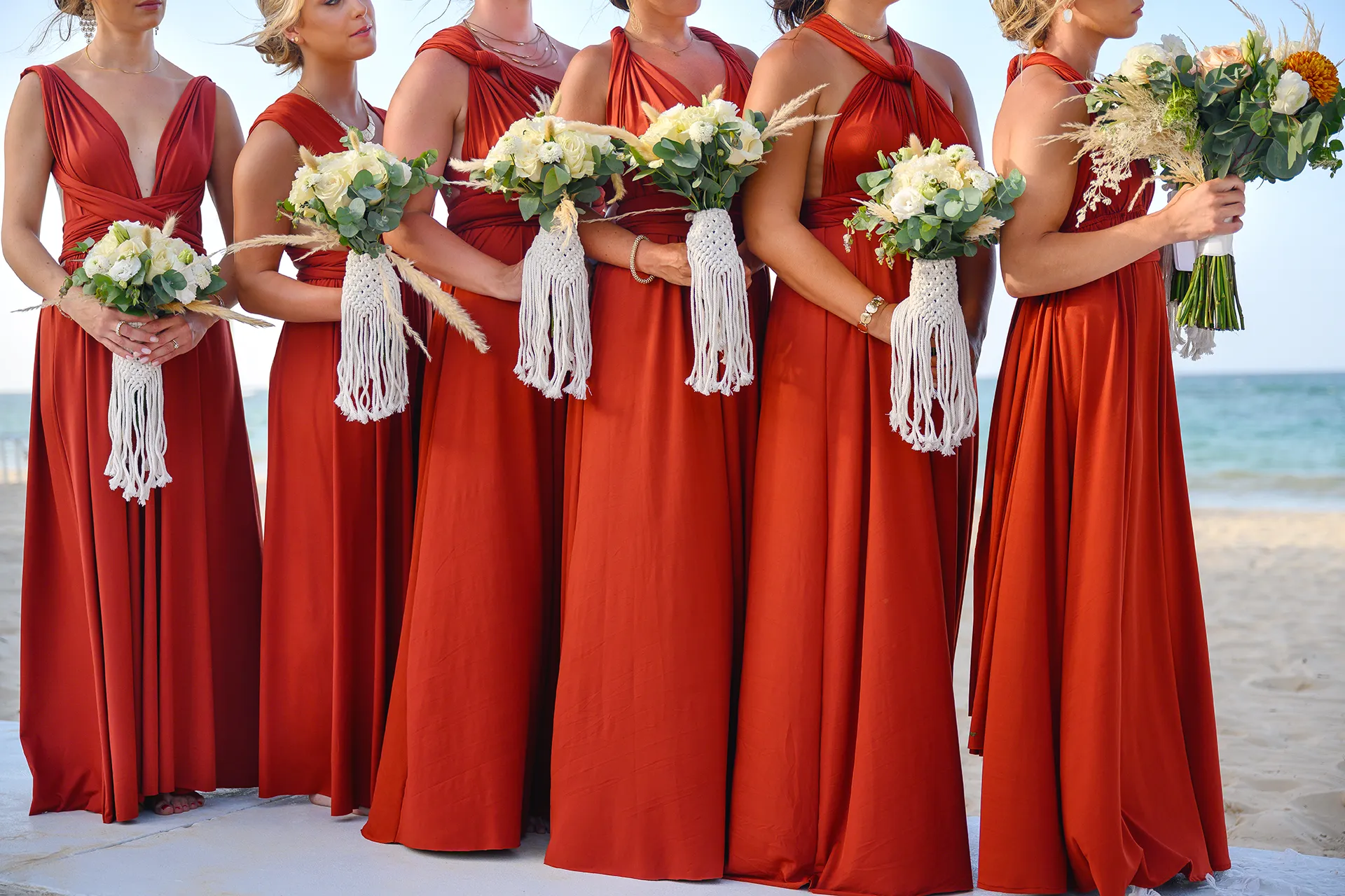 terracotta-bridesmaid-dresses-beach-wedding-punta-cana Bridesmaids in terracotta dresses holding bouquets with macrame wraps on the beach