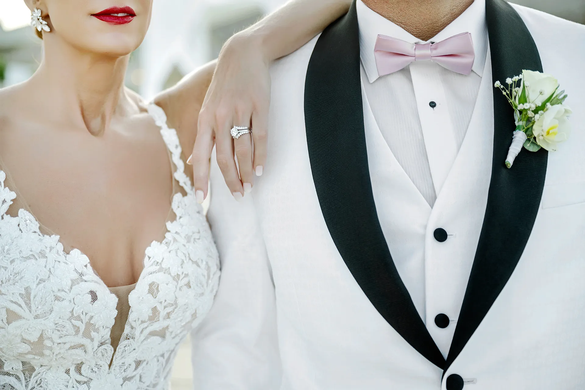 Bride resting her hand on the shoulder of a groom in a white shawl-collar dinner jacket and pink bow tie